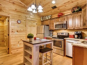 A wooden cabin kitchen with a central island, wooden cabinets, a microwave, a refrigerator, a stove, and a coffee maker.