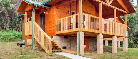 Una cabaña de madera con base de piedra, un porche y una escalera que conduce a la entrada.