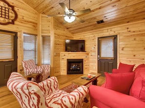 A cozy log cabin interior with a fireplace, wooden walls, and a ceiling fan. - Riverside | Pigeon Forge | Pet Friendly | Hot Tub | Arcade | WiFi (PIGEON FORGE)