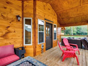 A wooden cabin with a porch, a red sofa, two red chairs, and a stone fireplace. - Riverside | Pigeon Forge | Pet Friendly | Hot Tub | Arcade | WiFi (PIGEON FORGE)