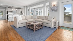A modern living room with a sectional sofa, a coffee table, and a kitchen in the background. - Welcome to BIS BALD!, your Oceanfront Escape on BHI! (Bald Head Island)