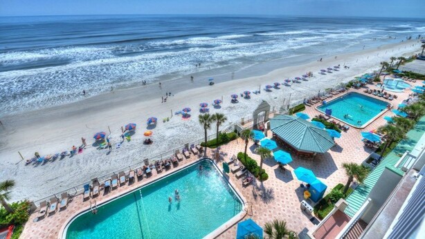 A beach resort with a swimming pool, beach umbrellas, and lounge chairs. - Oceanfront Retreat- Poolside View- Budget Friendly (Daytona Beach)