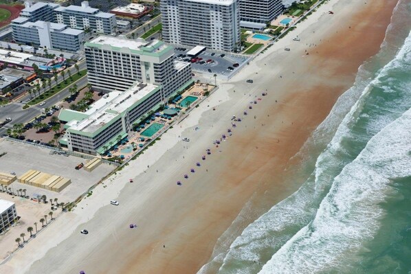 An aerial view of a beachside hotel with multiple buildings, a sandy beach, and a pool area.