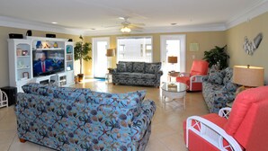 A living room with a television, two sofas, a red armchair, and a ceiling fan. - This is it! Spacious Luxury 8 Bedroom Villa, Pool, Hs Internet (North Myrtle Beach)