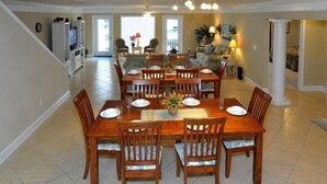 A spacious dining area with a large wooden table and chairs, a kitchen in the background, and a staircase leading to another level. - This is it! Spacious Luxury 8 Bedroom Villa, Pool, Hs Internet (North Myrtle Beach)