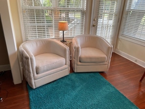 A room with two beige armchairs, a teal rug, and a lamp on a small table.