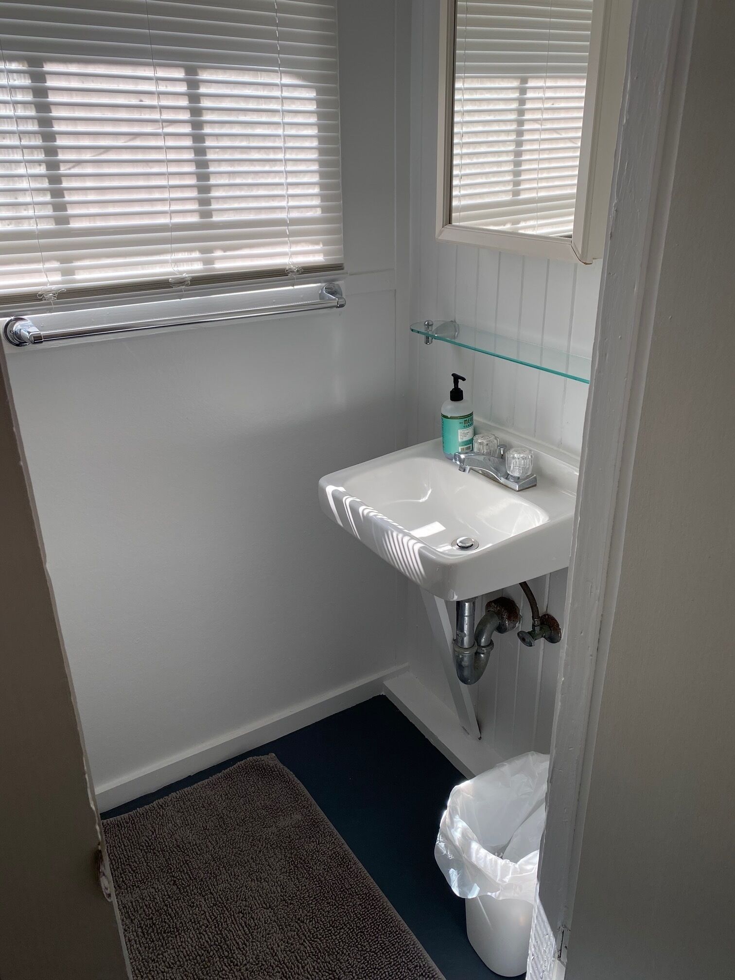 Ein kleines, sauberes Badezimmer mit einem weißen Waschbecken, einer Glasablage und einer Toilette.