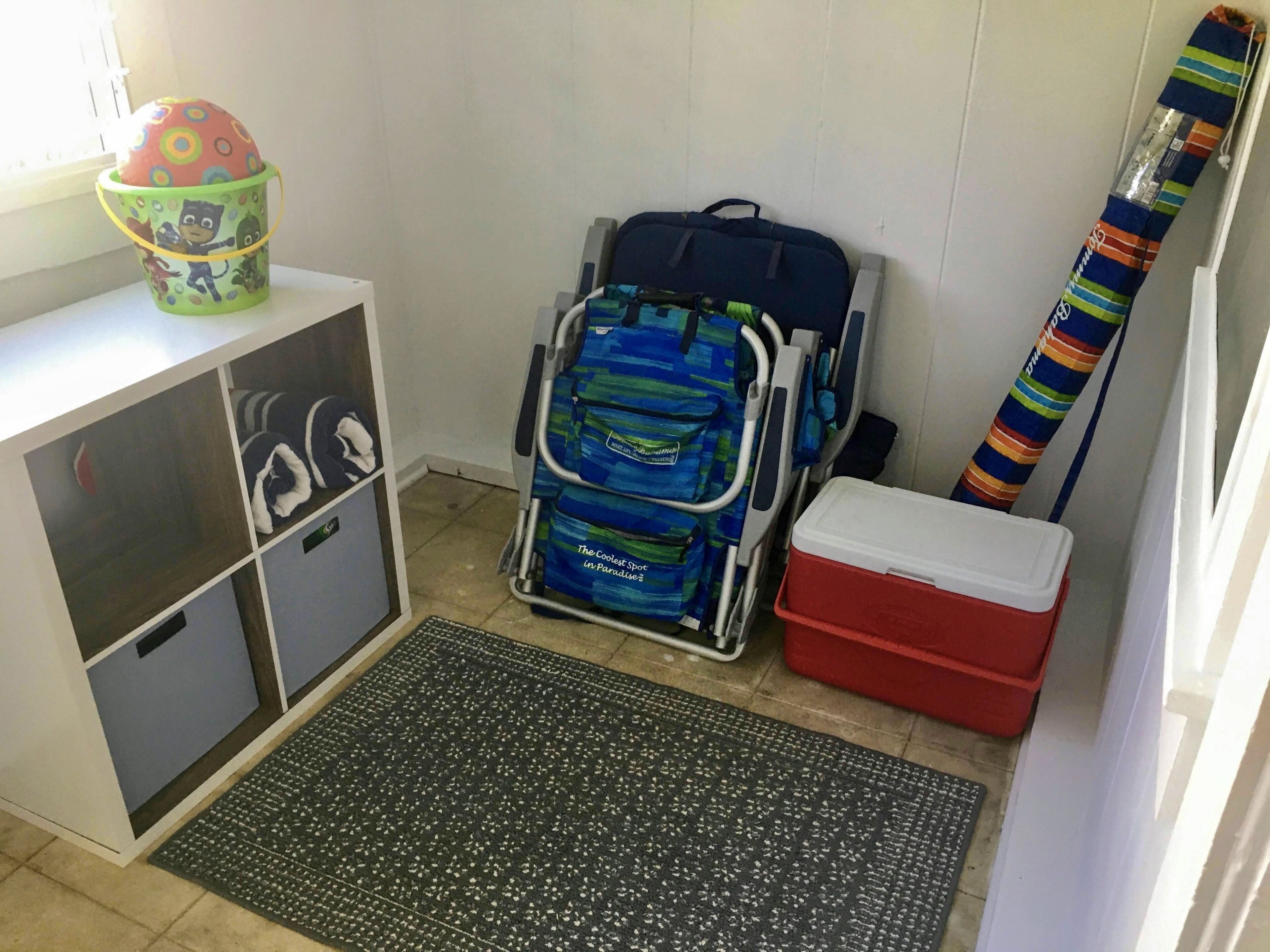 A storage area with a metal cart, a red cooler, and a colorful striped item leaning against the wall.