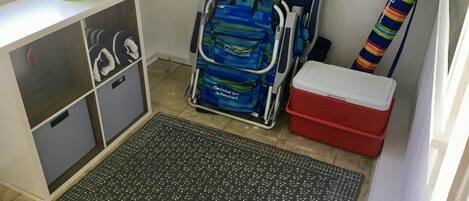A storage area with a metal cart, a red cooler, and a colorful striped item leaning against the wall.