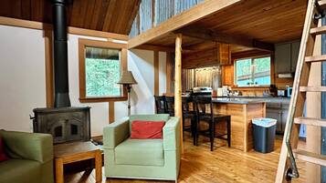 Un intérieur de chalet chaleureux avec un plancher en bois, un canapé, un coin repas et une cuisine.