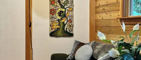 A cozy room with a wooden ceiling, a wall-mounted air conditioner, a green sofa with cushions, a framed floral tapestry, and a wooden cabinet with a mirror.