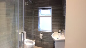 A bathroom with a glass shower enclosure, a toilet, a sink, and a window providing natural light. - The White House 7 DOUBLE BED HOUSE FULLY-EQUIPPED (London)