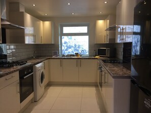 A modern kitchen with a built-in washer and dryer, a microwave, and a large window providing natural light. - The White House 7 DOUBLE BED HOUSE FULLY-EQUIPPED (London)