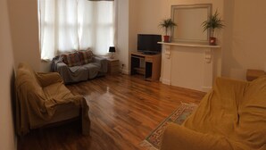 A living room with a sofa, a television, and a fireplace with two potted plants. - The White House 7 DOUBLE BED HOUSE FULLY-EQUIPPED (London)