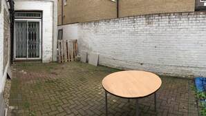 A courtyard with a round table, a white brick wall, and a metal gate. - The White House 7 DOUBLE BED HOUSE FULLY-EQUIPPED (London)