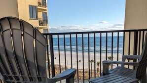 A balcony with two chairs and a small table, overlooking a beach with a clear view of the ocean and a building in the background. - Beach, Sand, Shells, And An Ocean As Far As You Can See At Our Cozy Condo in PCB (Panama City)
