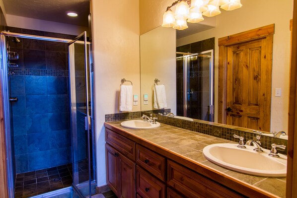 A bathroom with two sinks, a glass shower enclosure, and a wooden door.