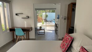 Un dormitorio con cama, escritorio, silla y vistas a un patio exterior.