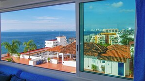 A room with a large window offering a view of the sea and a cityscape.