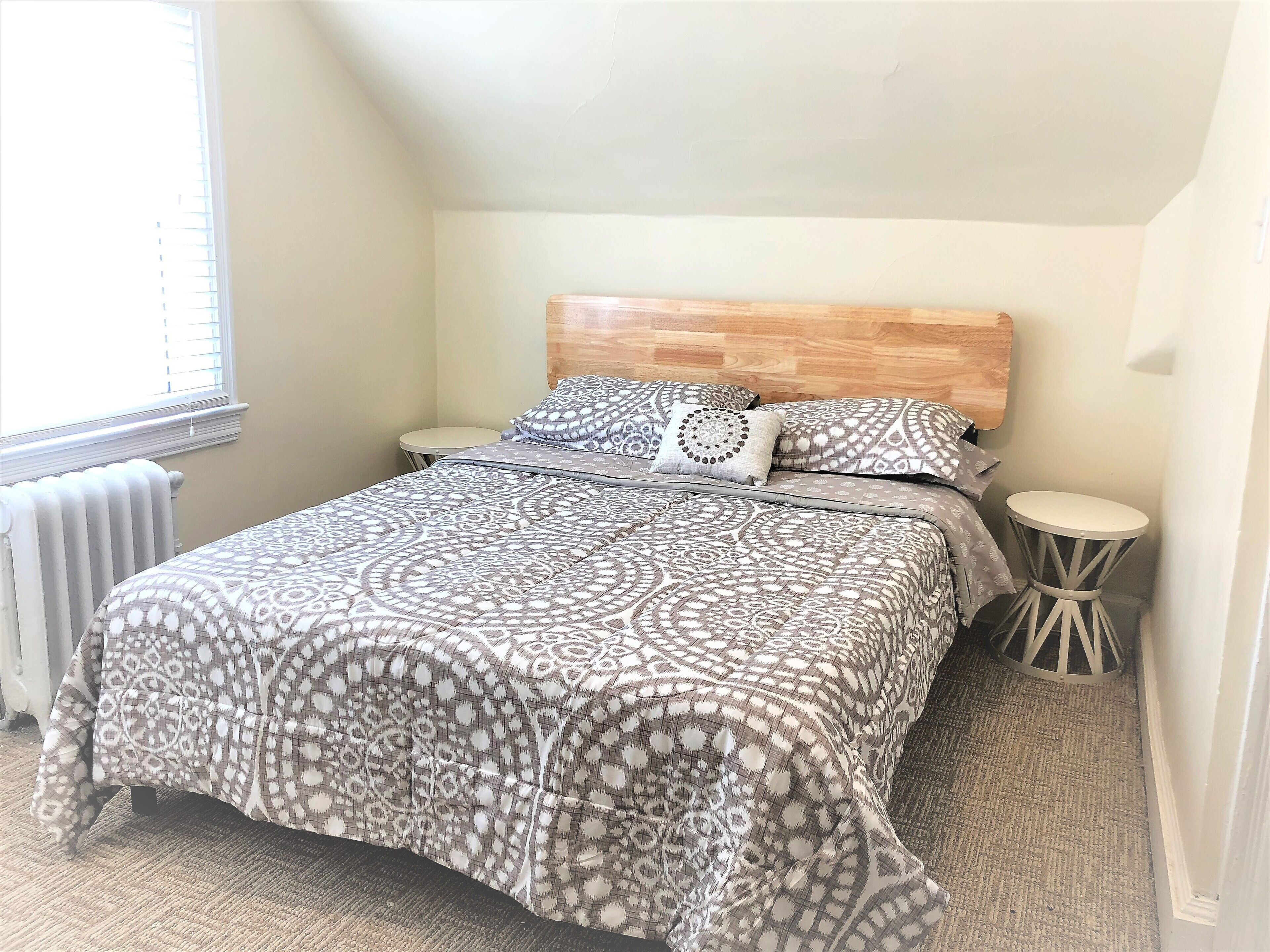 Quarto com colcha estampada, duas mesas de cabeceira, painel de cama de madeira e radiador.