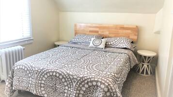 Quarto com colcha estampada, duas mesas de cabeceira, painel de cama de madeira e radiador.
