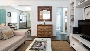 Una sala de estar con sofá, mesa de centro, cómoda de madera, mueble para televisión y espejo.
