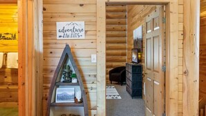 A wooden interior with a sign reading 'adventure awaits,' a shelf with decorative items, and a hallway leading to a door. - Bear Tracks - 20 Miles to Yellowstone - Air Condition - Wifi (Island Park)