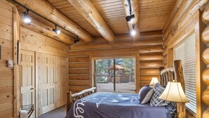A log cabin bedroom with a bed, a nightstand, a lamp, and a window. - Bear Tracks - 20 Miles to Yellowstone - Air Condition - Wifi (Island Park)