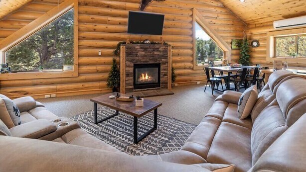A log cabin interior with a fireplace, leather sofa, dining table, and large windows. - Bear Tracks - 20 Miles to Yellowstone - Air Condition - Wifi (Island Park)