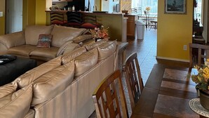 A living room with a beige sofa, wooden dining table, and chairs. There is a kitchen area with cabinets and a refrigerator in the background. - Golf ... Bird Watching, Biking, Hiking, Sunsets, Star Gazing ... Oh, great Golf (Green Valley)