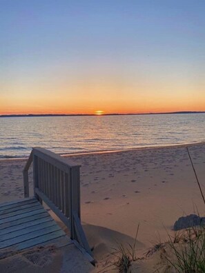 A wooden boardwalk leading to a sandy beach with a sunset in the background.