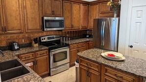 A kitchen with wooden cabinets, a stainless steel refrigerator, a microwave, a stove, and granite countertops. - Top Floor Legacy Penthouse / Stunning Gulf Views / Walk to Beach, Pools & more! (Gulfport)