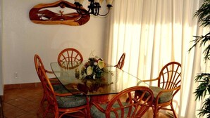 Un coin repas avec une table en verre entourée de chaises en osier, un lustre et une fenêtre agrémentée de rideaux.