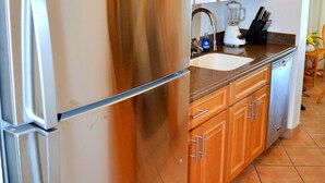 Une cuisine avec des meubles de rangement en bois, un réfrigérateur en acier inoxydable, un évier et un plan de travail sur lequel se trouvent un mixeur et un bloc à couteaux.