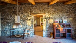 A rustic interior with stone walls, wooden beams, a hanging lamp, a cabinet with glass doors, and a chair. - Tuscan Stone Farmhouse for 16 guests, amazing view, vineyards and olive trees (Manciano)
