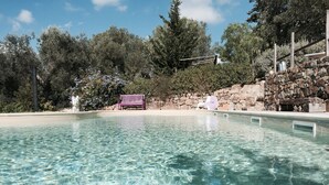 A clear swimming pool with a stone wall and a wooden deck. - Tuscan Stone Farmhouse for 16 guests, amazing view, vineyards and olive trees (Manciano)