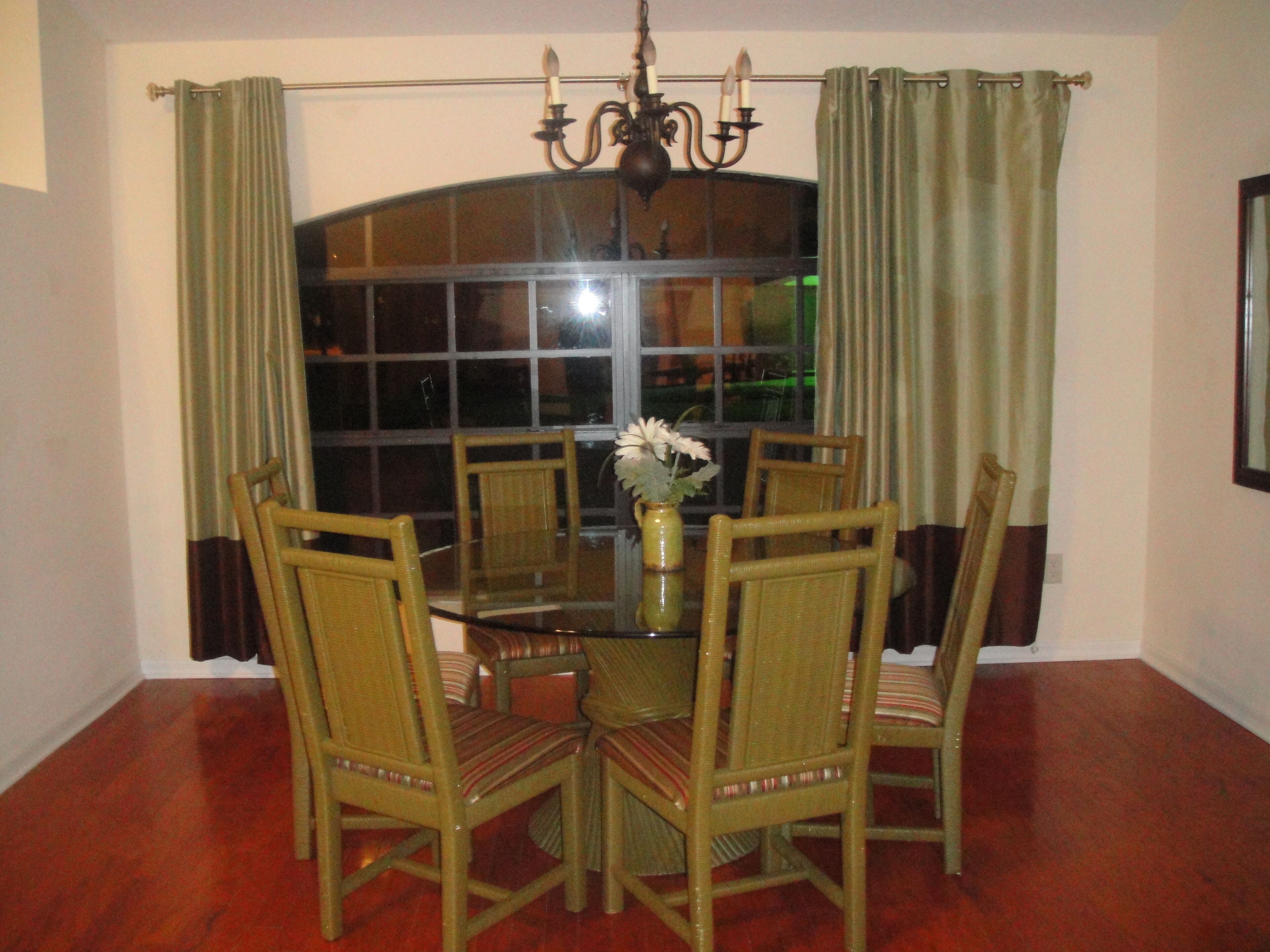 Uma área de refeições com mesa de vidro, cadeiras de vime, um vaso com flores e um candelabro.