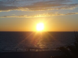 A sunset over the ocean with silhouettes of people on the beach.