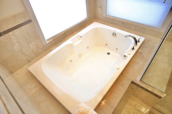 A large, rectangular bathtub with a chrome faucet and control panel, situated in a bathroom with beige tiled flooring and walls. - Luxury Smart System Enabled Home on the Hill with Beautiful View (Happy Valley)