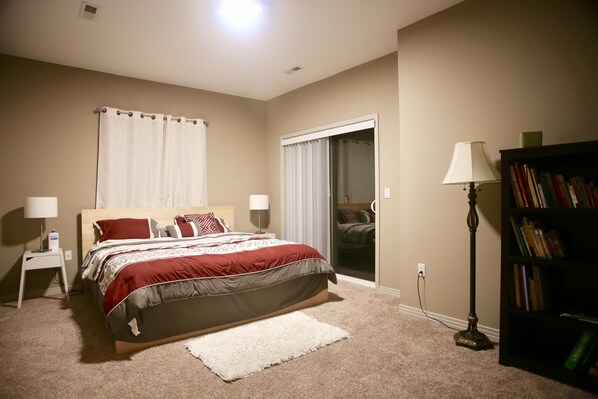 A bedroom with a bed, bedside lamps, a bookshelf, and a door leading to a balcony. - Luxury Smart System Enabled Home on the Hill with Beautiful View (Happy Valley)