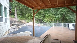 Une terrasse couverte agrémentée d’une cascade en pierre, entourée d’une terrasse en bois et d’une clôture blanche.