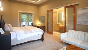 Une chambre à coucher comprenant un lit, un bureau, une chaise, un canapé blanc et une salle de bain visible à travers une porte en verre.