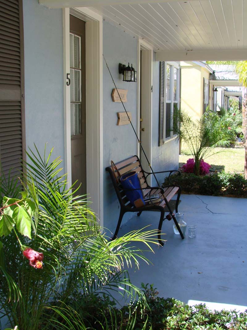 A porch with a bench, a door, and a small garden area with plants and flowers.