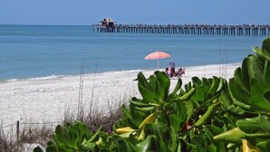 A beach with a pier extending into the water, a few people on the sand, and an umbrella. - Naples Vanderbilt Beach-beautiful Updated-walk to the beach (Naples)