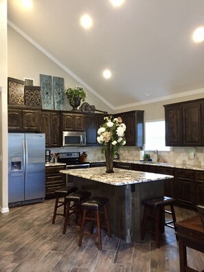 A modern kitchen with dark wood cabinets, a central island with stools, stainless steel appliances, and decorative wall art.