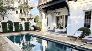 A swimming pool with a clear view of the surrounding architecture, including a covered patio area with outdoor furniture and a view of neighboring buildings.