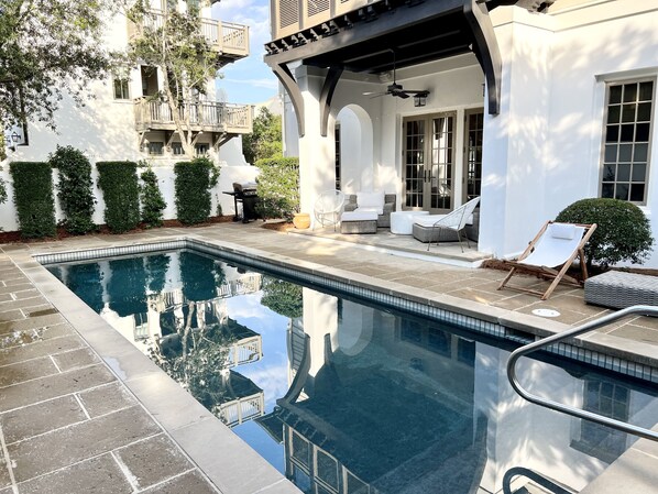 Una piscina con vista despejada a la arquitectura circundante, incluyendo un patio cubierto con mobiliario exterior y vistas a edificios vecinos.