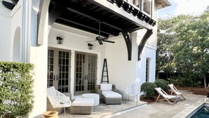 A covered outdoor seating area with wicker furniture and a pool.