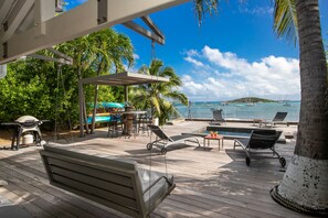 A wooden deck with lounge chairs, a barbecue grill, and a poolside area overlooking the ocean with boats. - every morning turn your dream into reality in front of Pinel Island (SAINT MARTIN)
