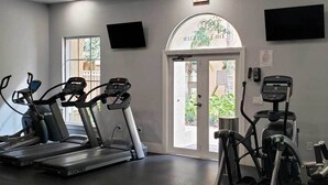 A gym with treadmills and elliptical machines, a TV mounted on the wall, and a door leading outside.